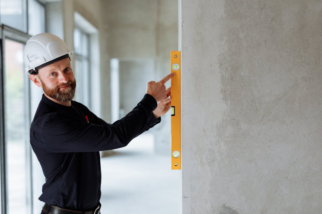 Confident engineer with hard hat using a spirit level on a wall at a construction site.